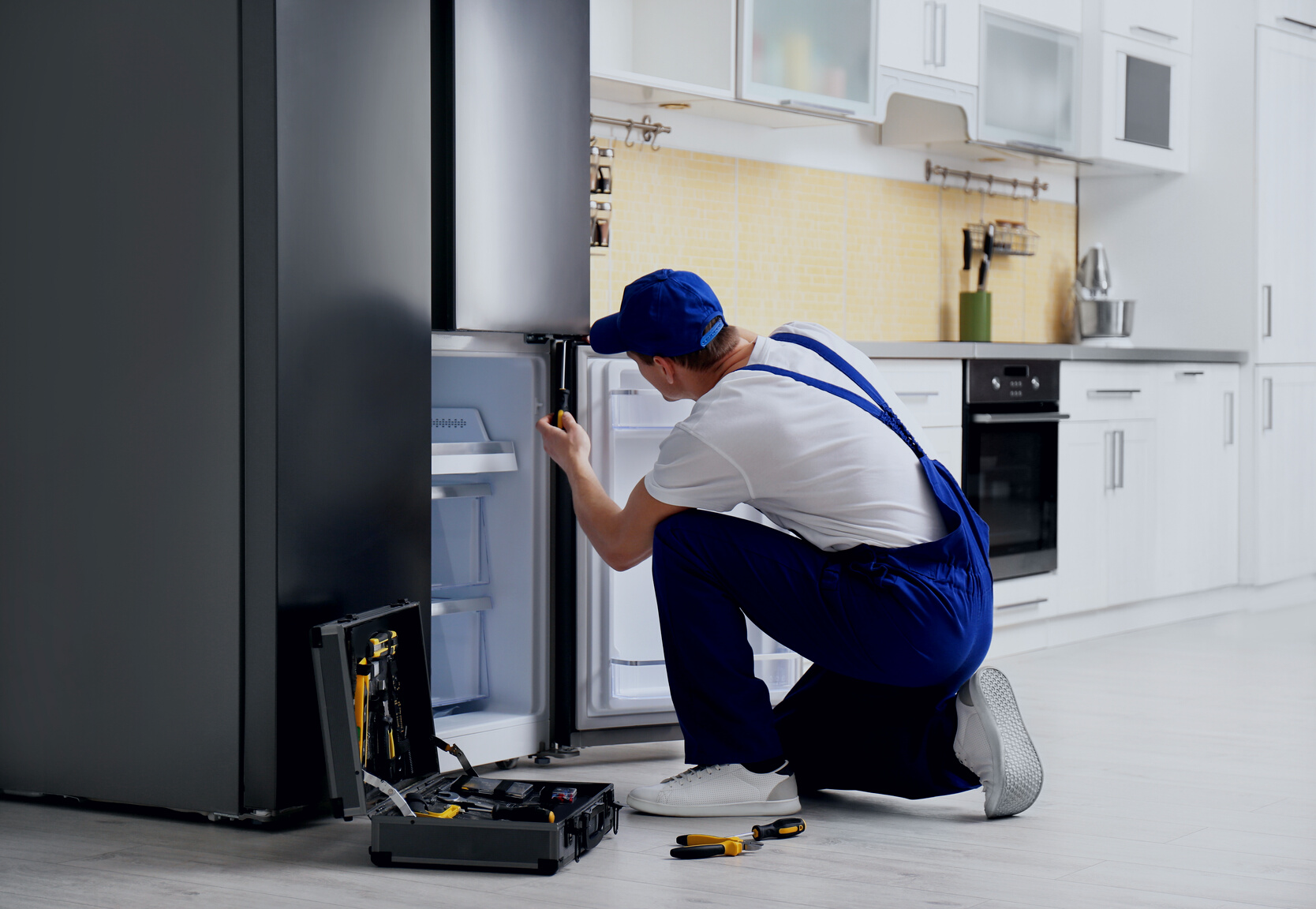 Male Technician with Screwdriver Repairing Refrigerator in Kitchen